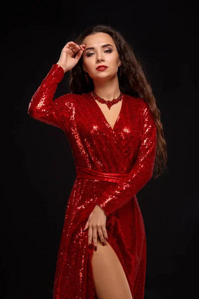 Charming young caucasian brunette woman in red cocktail dress posing before camera on black background — Stock Photo, Image