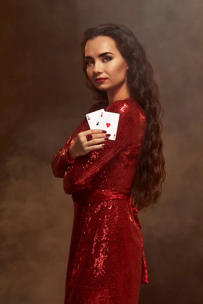 Young beautiful lucky brunette in a red evening dress shows her cards, a pair of aces — Stock Photo, Image