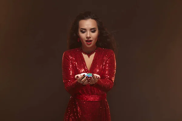 Giovane donna bruna piuttosto fortunata in un abito da sera rosso tiene chip di poker nelle sue mani, mostrando le sue vincite . — Foto Stock