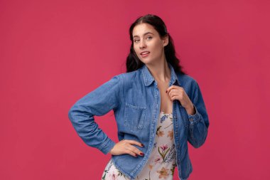 Stüdyoda pembe arka plan üzerinde duran açık bir elbise ve mavi gömlek güzel bir genç kadının portresi. İnsanlar samimi duygular.