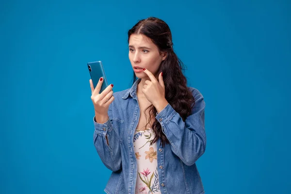 Junge brünette Frau posiert mit einem Smartphone auf blauem Hintergrund. — Stockfoto