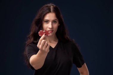 Kıvırcık saçlı esmer elinde kırmızı kumar cipsi ile poz veriyor. Siyah bir arka plan üzerinde Poker kavramı. Casino.