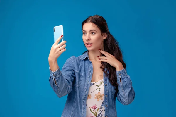 Junge brünette Frau posiert mit einem Smartphone auf blauem Hintergrund. — Stockfoto
