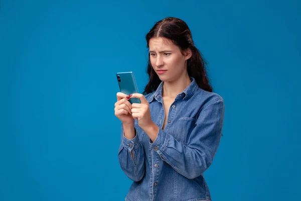 Молодая брюнетка позирует со смартфоном на синем фоне . — стоковое фото
