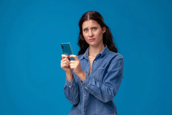 Junge brünette Frau posiert mit einem Smartphone auf blauem Hintergrund. — Stockfoto