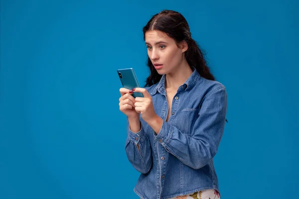 Junge brünette Frau posiert mit einem Smartphone auf blauem Hintergrund. — Stockfoto