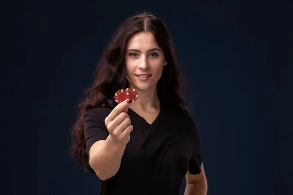 Σγουρά μαλλιά μελαχρινή ποζάρει με κόκκινα τσιπ τζόγου στα χέρια της. Η ιδέα του πόκερ σε μαύρο φόντο. Καζίνο. — Φωτογραφία Αρχείου
