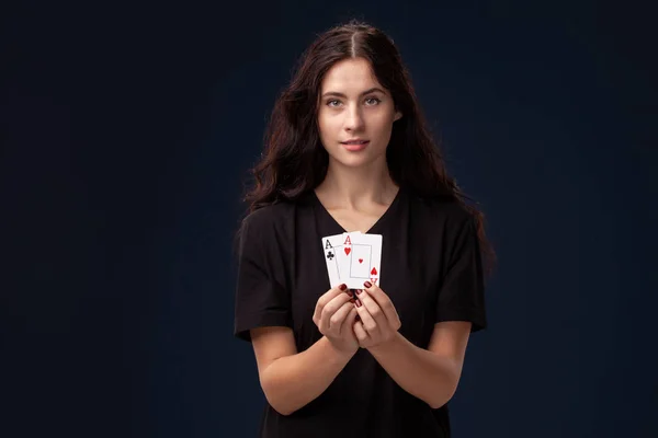 Curly hair brunette is posing with playing cards in her hands. Poker concept on a black background. Casino.