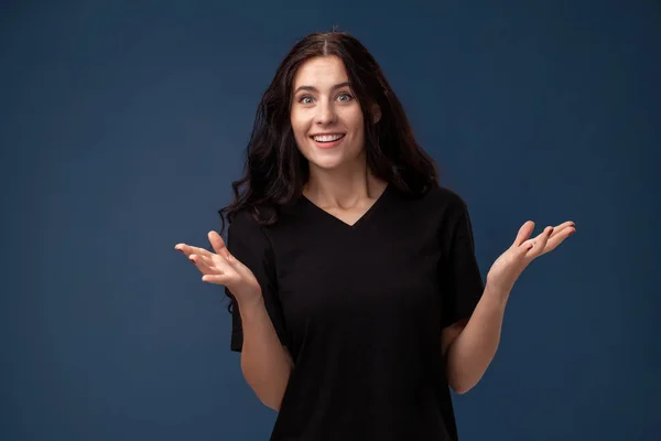 Retrato de una morena de pelo largo en camiseta negra posando sobre un fondo gris y mostrando diferentes emociones . — Foto de Stock