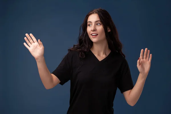 Retrato de uma mulher morena de cabelos longos em camiseta preta posando em um fundo cinza e mostrando emoções diferentes . — Fotografia de Stock