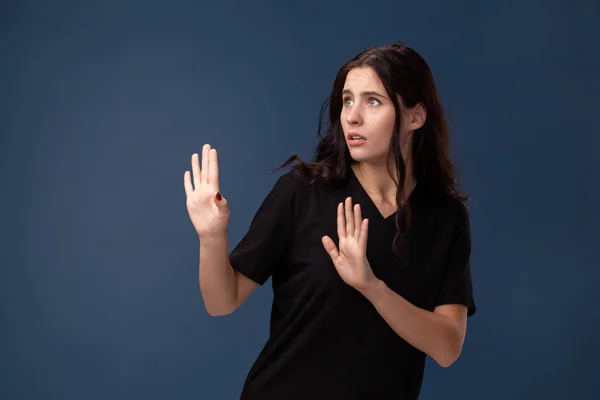 Retrato de una morena de pelo largo en camiseta negra posando sobre un fondo gris y mostrando diferentes emociones . —  Fotos de Stock