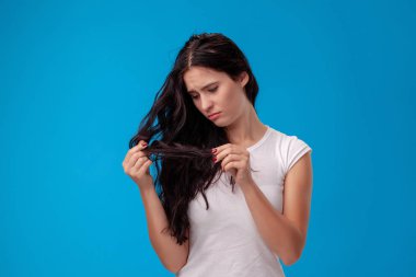Üzgün kadın mavi arka planda saçlarını çekiyor