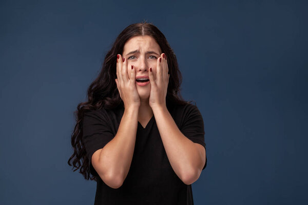Portrait of a long-haired brunette woman in black t-shirt posing on a gray background and showing different emotions.