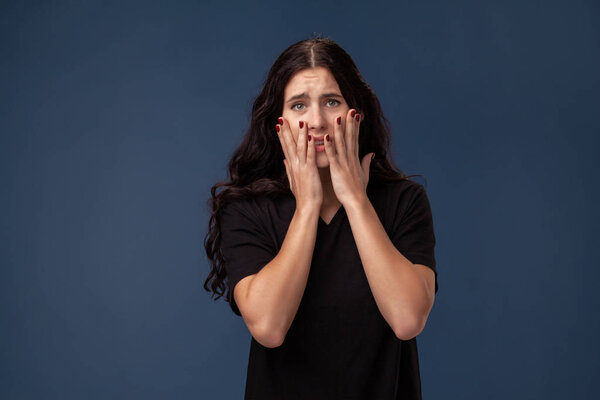 Portrait of a long-haired brunette woman in black t-shirt posing on a gray background and showing different emotions.
