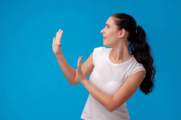 Retrato de estúdio de uma jovem mulher bonita em uma camiseta branca contra um fundo de parede azul. Pessoas emoções sinceras . — Fotografia de Stock