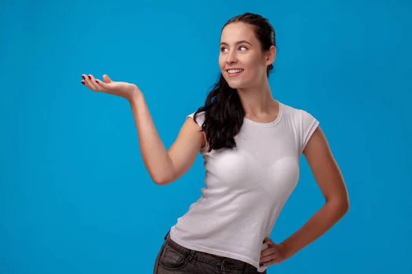 Retrato de estúdio de uma jovem mulher bonita em uma camiseta branca contra um fundo de parede azul. Pessoas emoções sinceras . — Fotografia de Stock