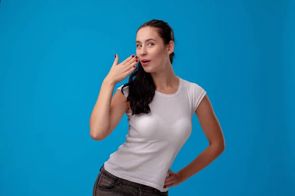 Στούντιο πορτρέτο μιας νεαρής όμορφης γυναίκας με ένα λευκό μπλουζάκι σε ένα μπλε φόντο τοίχου. Οι άνθρωποι ειλικρινή συναισθήματα. — Φωτογραφία Αρχείου