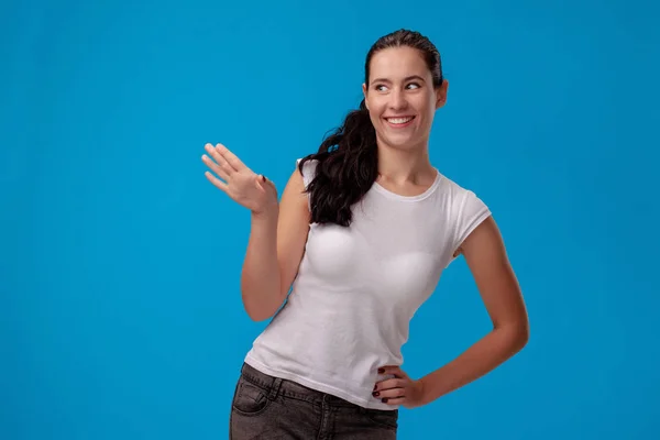 Studio portrait of a young beautiful woman in a white t-shirt against a blue wall background. People sincere emotions. — Stock Photo, Image