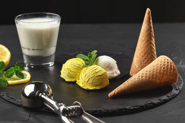 Nane ile süslenmiş lezzetli krem ve narenciye limonlu dondurma siyah bir arka plan üzerinde bir taş kayrak üzerinde servis.