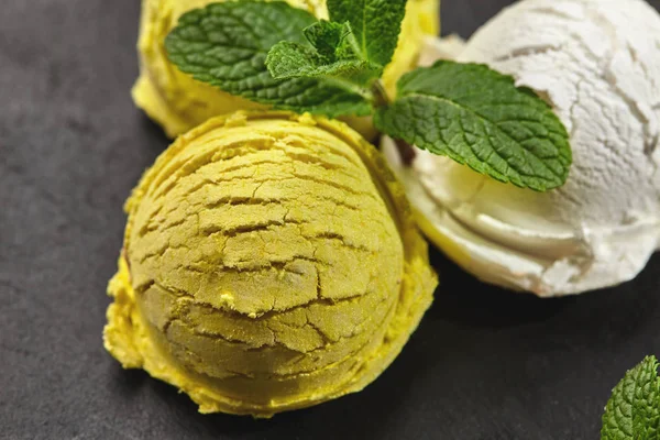 Tasty creamy and citrus lemon ice cream decorated with mint served on a stone slate over a black background.