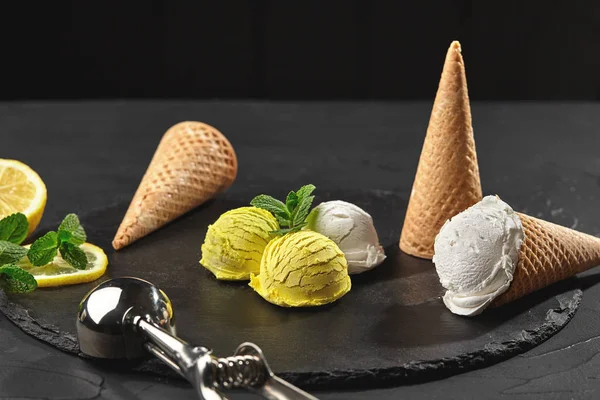 Tasty creamy and citrus lemon ice cream decorated with mint served on a stone slate over a black background. — Stock Photo, Image