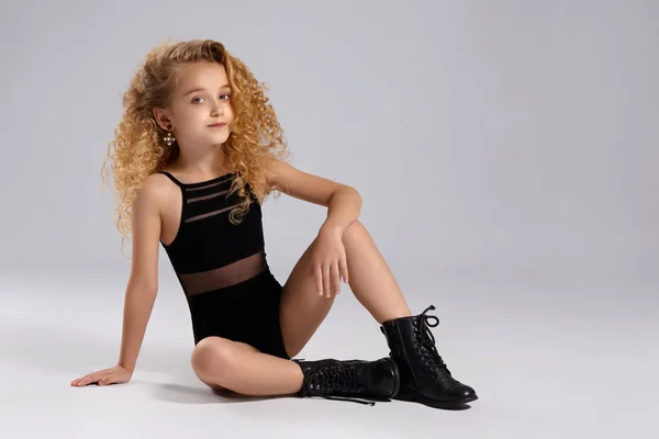 Bela ginasta menina em um maiô de esportes preto e botas em um fundo cinza . — Fotografia de Stock