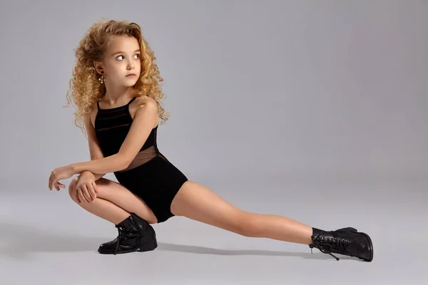 Hermosa niña gimnasta en un traje de baño deportivo negro y botas sobre un fondo gris . —  Fotos de Stock