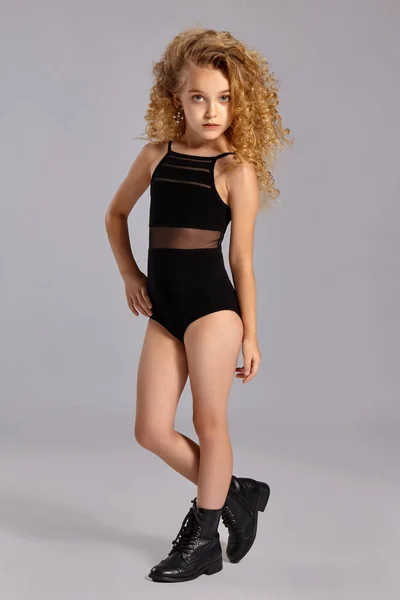 Krásná holčička gymnastka v černém sportovním obleku a botách na šedém pozadí. — Stock fotografie