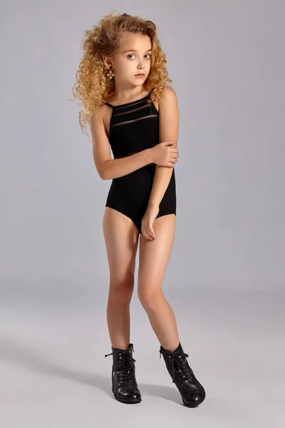 Gyönyörű kislány tornász egy fekete sport fürdőruhát és csizmát a szürke háttér. — Stock Fotó