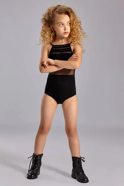 Beautiful little girl gymnast in a black sports swimsuit and boots on a gray background. — Stock Photo, Image