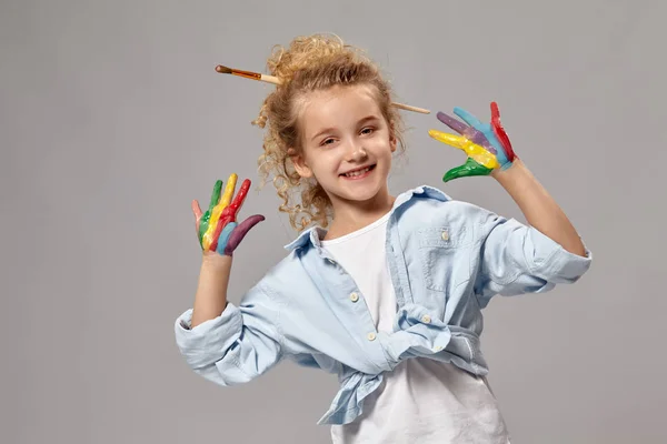 Mooi klein meisje met een geschilderde handen poseren op een grijze achtergrond. — Stockfoto