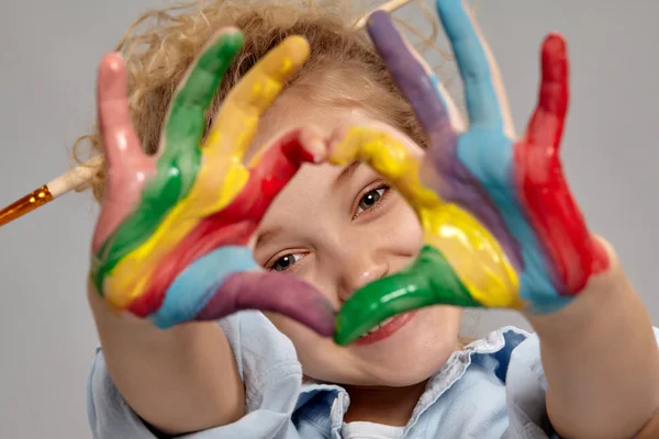 Mooi klein meisje met een geschilderde handen poseren op een grijze achtergrond. — Stockfoto