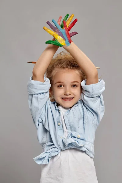 Mooi klein meisje met een geschilderde handen poseren op een grijze achtergrond. — Stockfoto