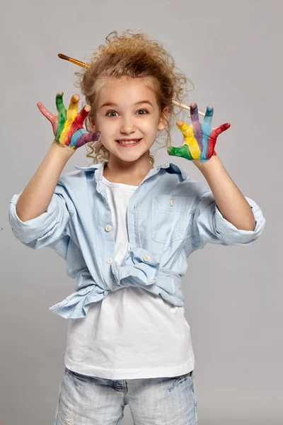 Mooi klein meisje met een geschilderde handen poseren op een grijze achtergrond. — Stockfoto