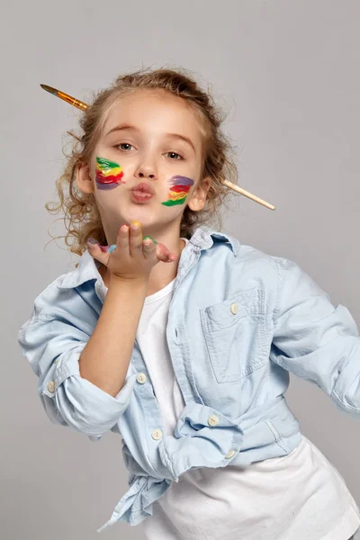 Hermosa niña con las manos y las mejillas pintadas posando sobre un fondo gris . —  Fotos de Stock