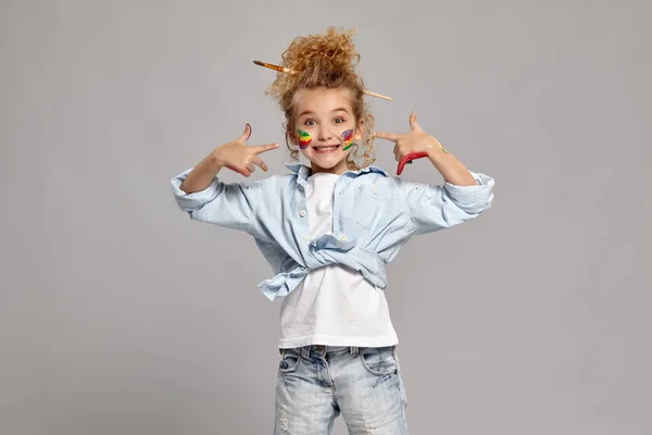 Hermosa niña con las manos y las mejillas pintadas posando sobre un fondo gris . —  Fotos de Stock