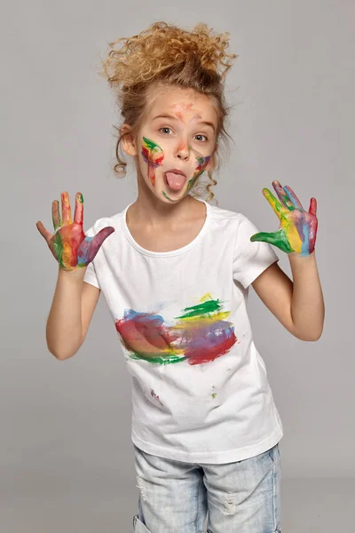 Beautiful little girl with a painted hands and cheeks is posing on a gray background. — Stock Photo, Image