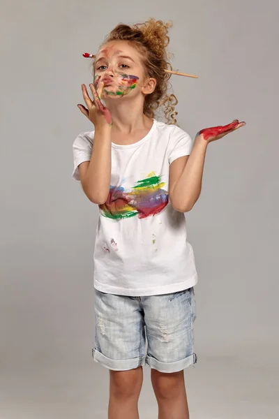 Beautiful little girl with a painted hands and cheeks is posing on a gray background. — Stock Photo, Image