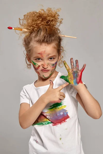 Hermosa niña con las manos y las mejillas pintadas posando sobre un fondo gris . —  Fotos de Stock