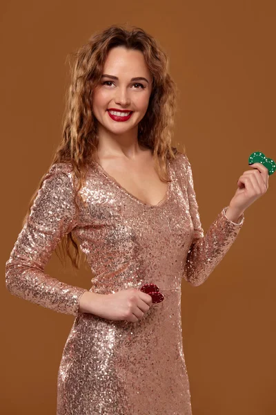 Blonďatá žena, která se dala do zlatých třpytaných šatů, drží v rukou nějaké barevné hráčské hranolky. Kasino. — Stock fotografie