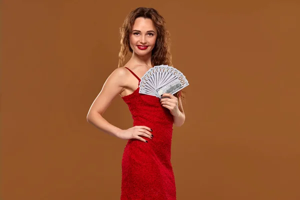 Blonďatá kudrnatá žena, v červených sexy šatech, drží v rukou sto dolarových bankovek. Kasino. — Stock fotografie