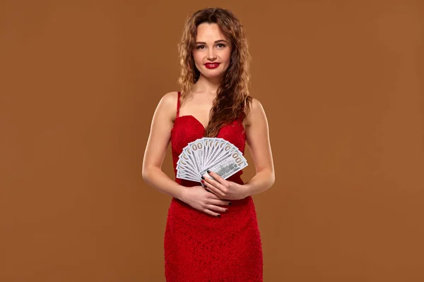 Bild einer glücklichen Frau mit braunen langen Haaren mit einem Fan von 100-Dollar-Scheinen, viel Bargeld, vor braunem Hintergrund — Stockfoto