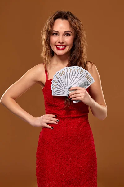 Obraz szczęśliwej szczęśliwej kobiety z brązowymi długimi włosami z fanem 100 dolarów banknotów, dużo gotówki, na brązowym tle — Zdjęcie stockowe