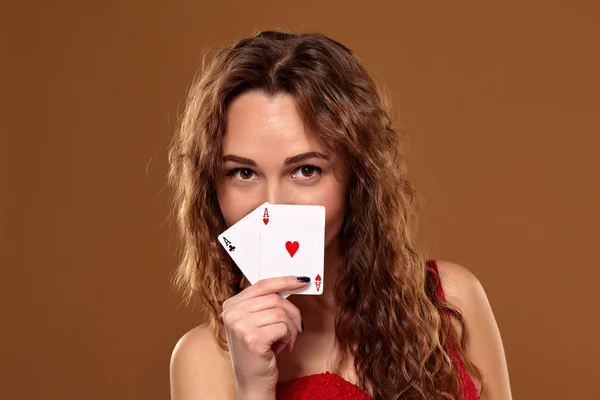 Mulher de cabelos castanhos bonita em vestido de cocktail vermelho segurando par de ases e sorrindo — Fotografia de Stock