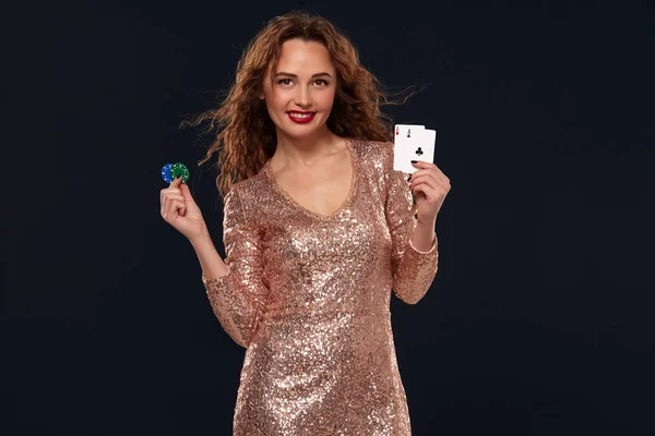 Hnědovlasá, atraktivní mladá žena ve zlatých koktejlových šatech v kasinu má dvě esa a hranolky v dlaních — Stock fotografie