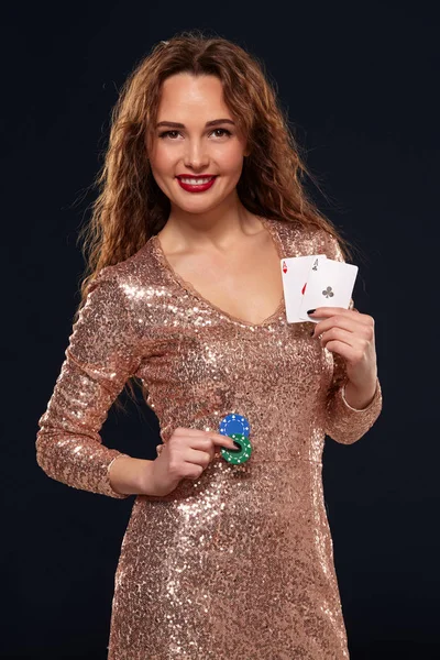 Bruna attraente giovane donna caucasica in abito da cocktail d'oro al casinò tiene un paio di assi e patatine nelle sue mani — Foto Stock