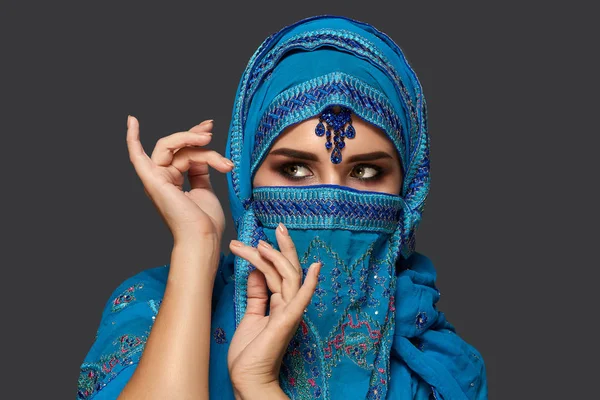 Studio shot of a young beautiful woman wearing the blue hijab decorated with sequins and jewelry. Arabic style. — Stock Photo, Image