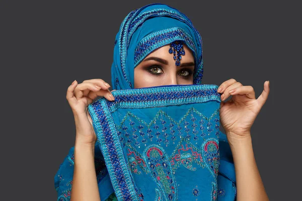 Studio shot van een jonge mooie vrouw het dragen van de blauwe hijab versierd met pailletten en sieraden. Arabische stijl. — Stockfoto