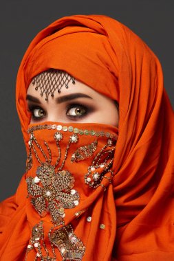 Payetler ve takılar ile süslenmiş terracotta hijab giyen genç bir büyüleyici kadın stüdyo çekim. Arap tarzı.