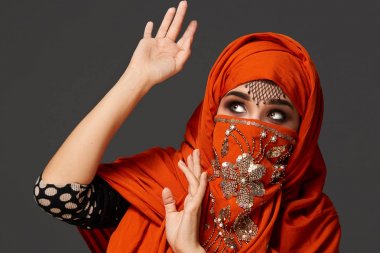 Payetler ve takılar ile süslenmiş terracotta hijab giyen genç bir büyüleyici kadın stüdyo çekim. Arap tarzı.